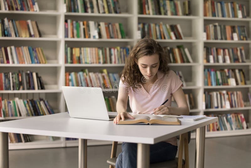 College student writing notes beside a laptop in a library study space